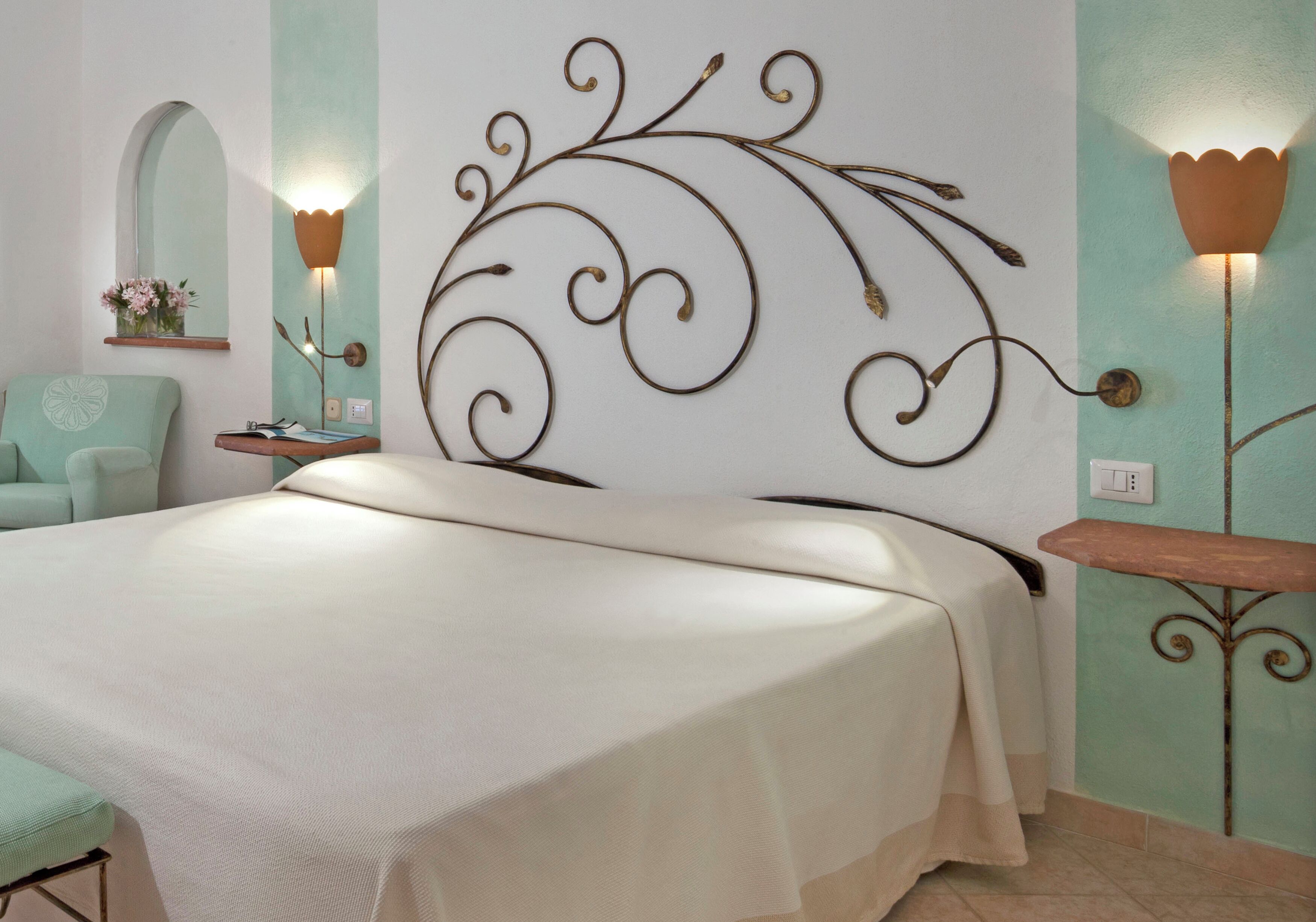 A bed with a decorative headboard, a bedside table, a chair, and a wall-mounted light fixture.