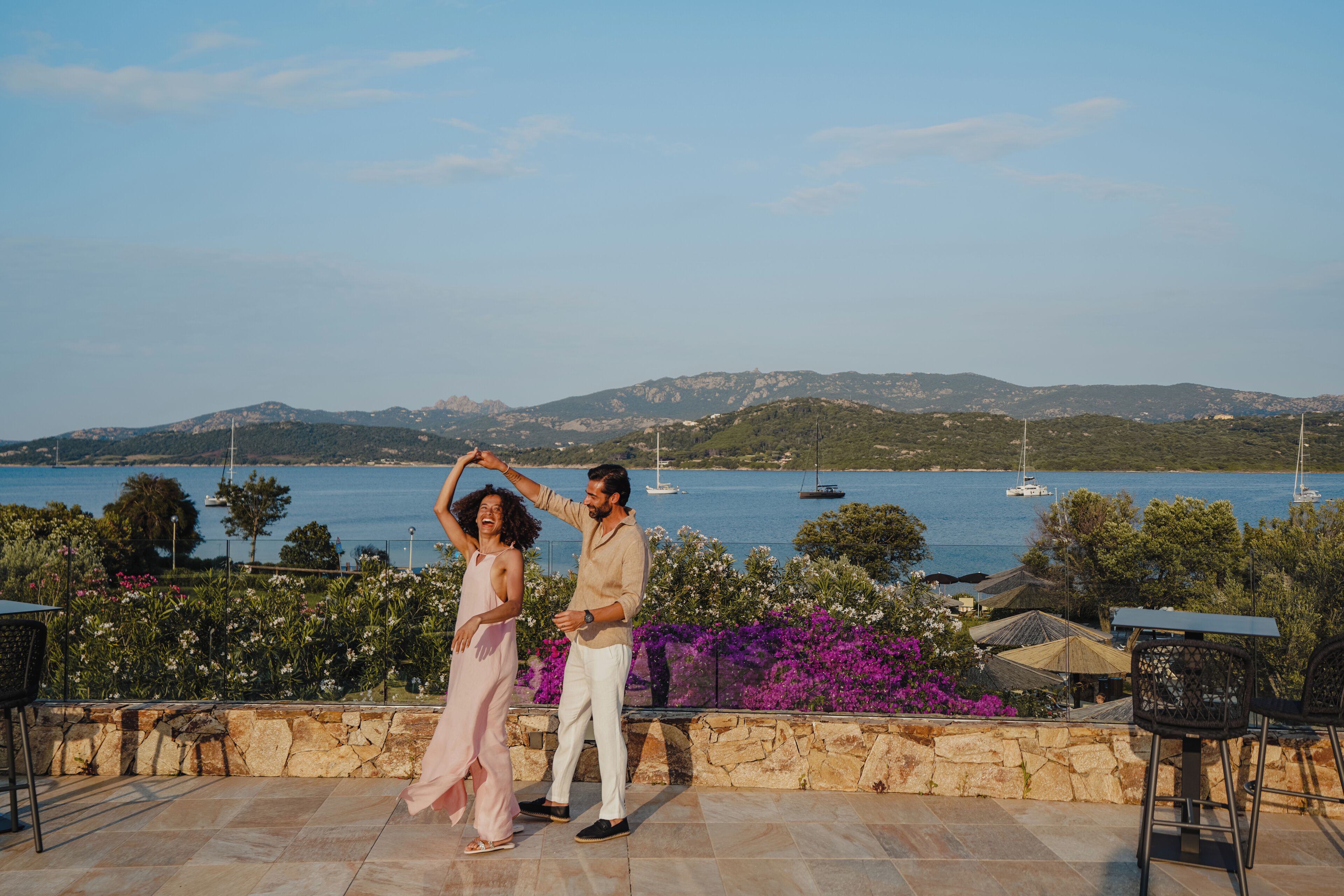 Una pareja bailando en una terraza con vistas al mar y a las montañas.