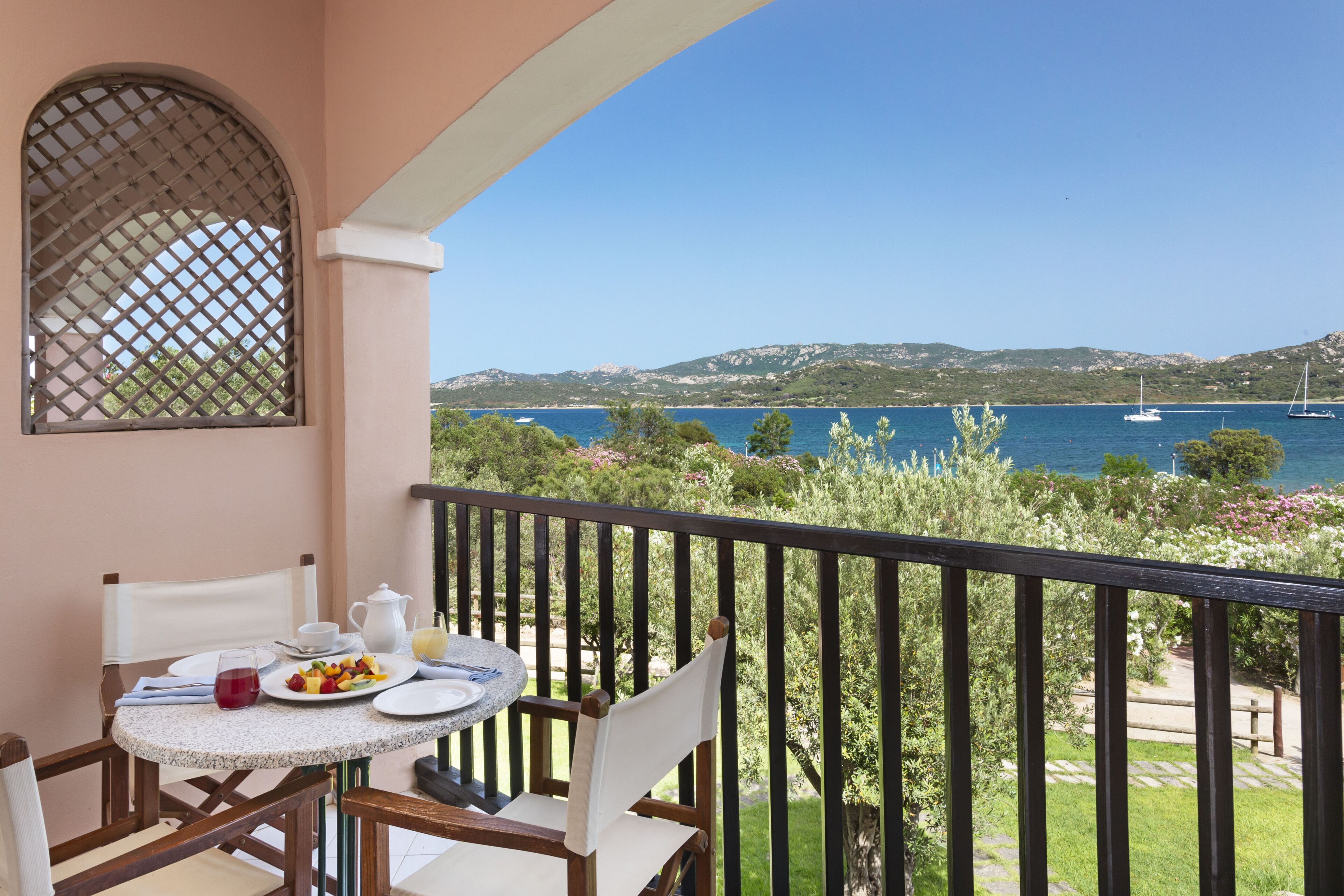 Un balcón con una mesa dispuesta para el desayuno, con vista a un cuerpo de agua y colinas.