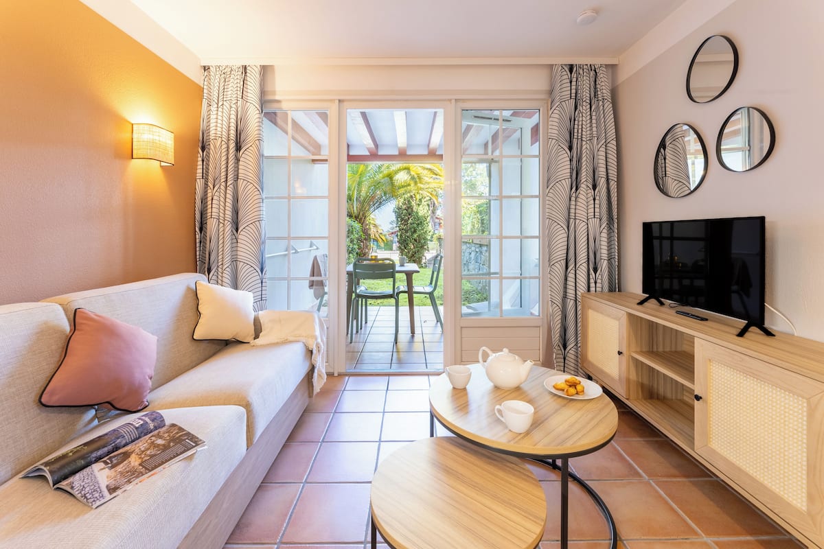 Een gezellige woonkamer met een bank, een klein tafeltje met theeservies, een televisie en uitzicht op een tuin door een schuifdeur.