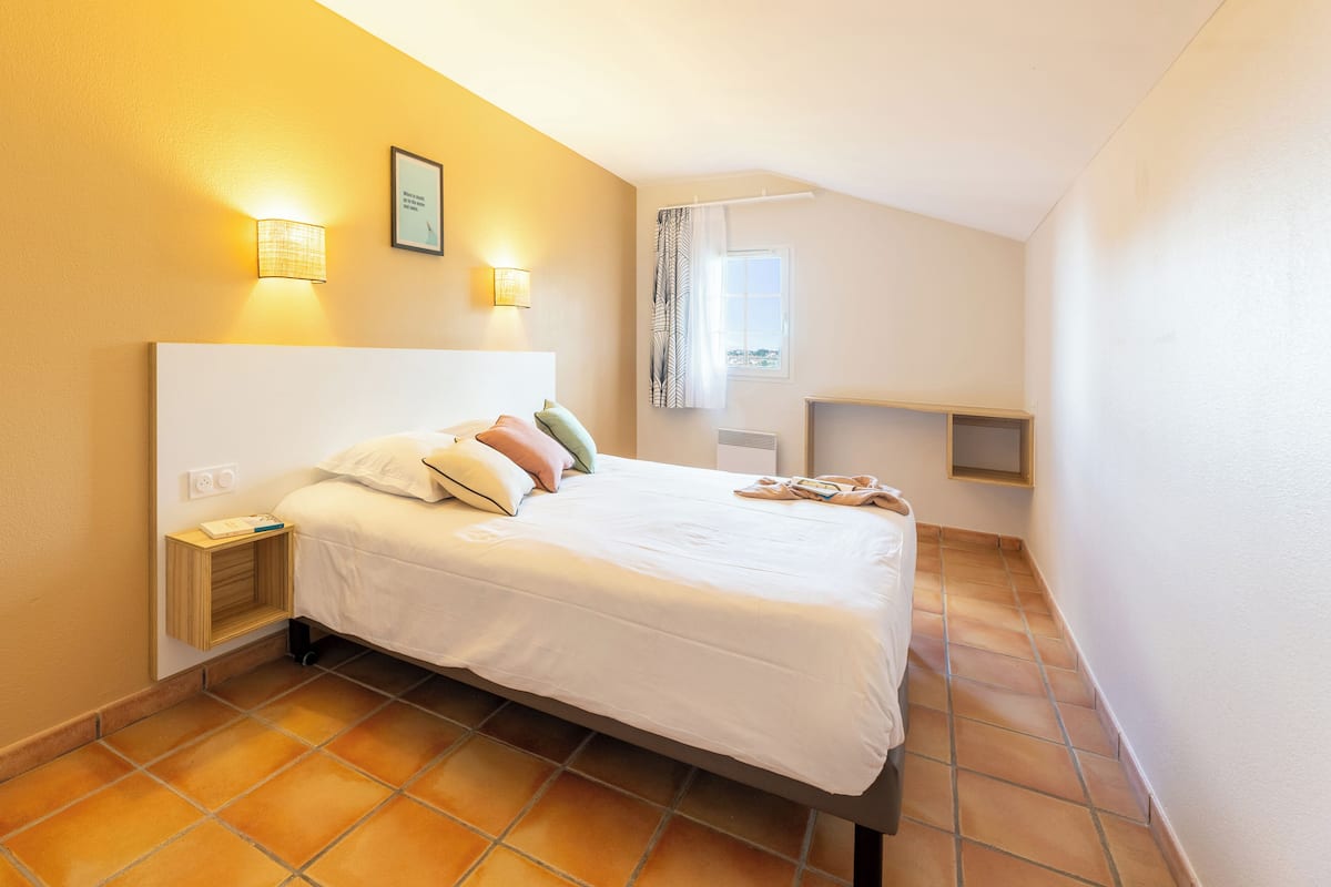 Een slaapkamer met een bed, nachtlampjes, een nachtkastje, een raam met gordijnen en uitzicht op de stad.