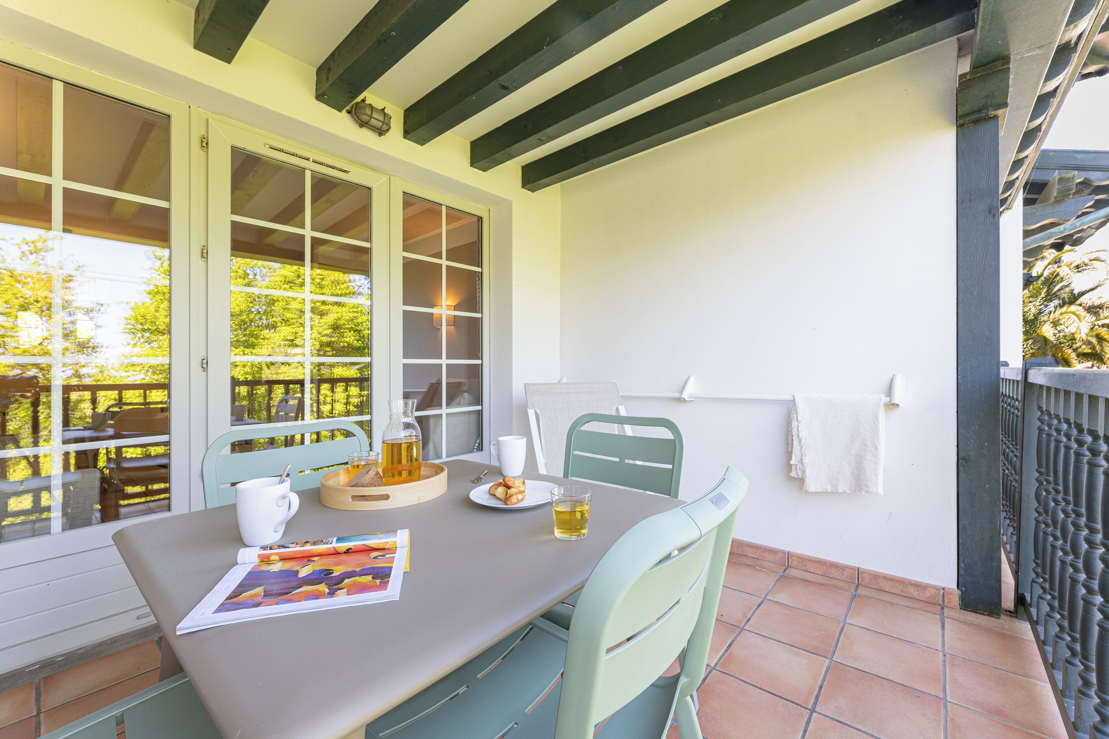 A patio with a table set for two, featuring a white mug, a glass of beer, and a plate of cookies.