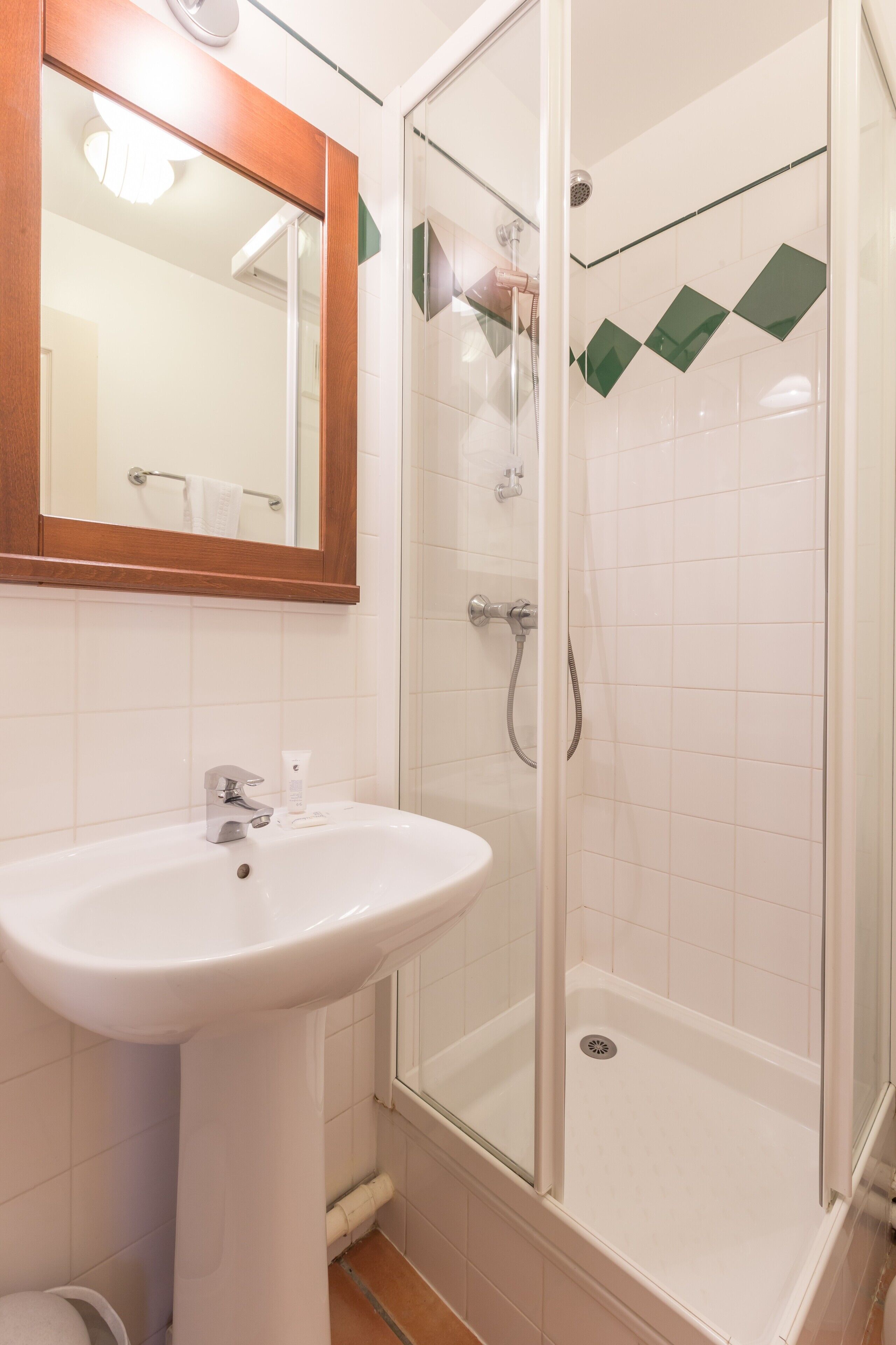 Un baño con lavamanos blanco, espejo y ducha con mampara de vidrio.