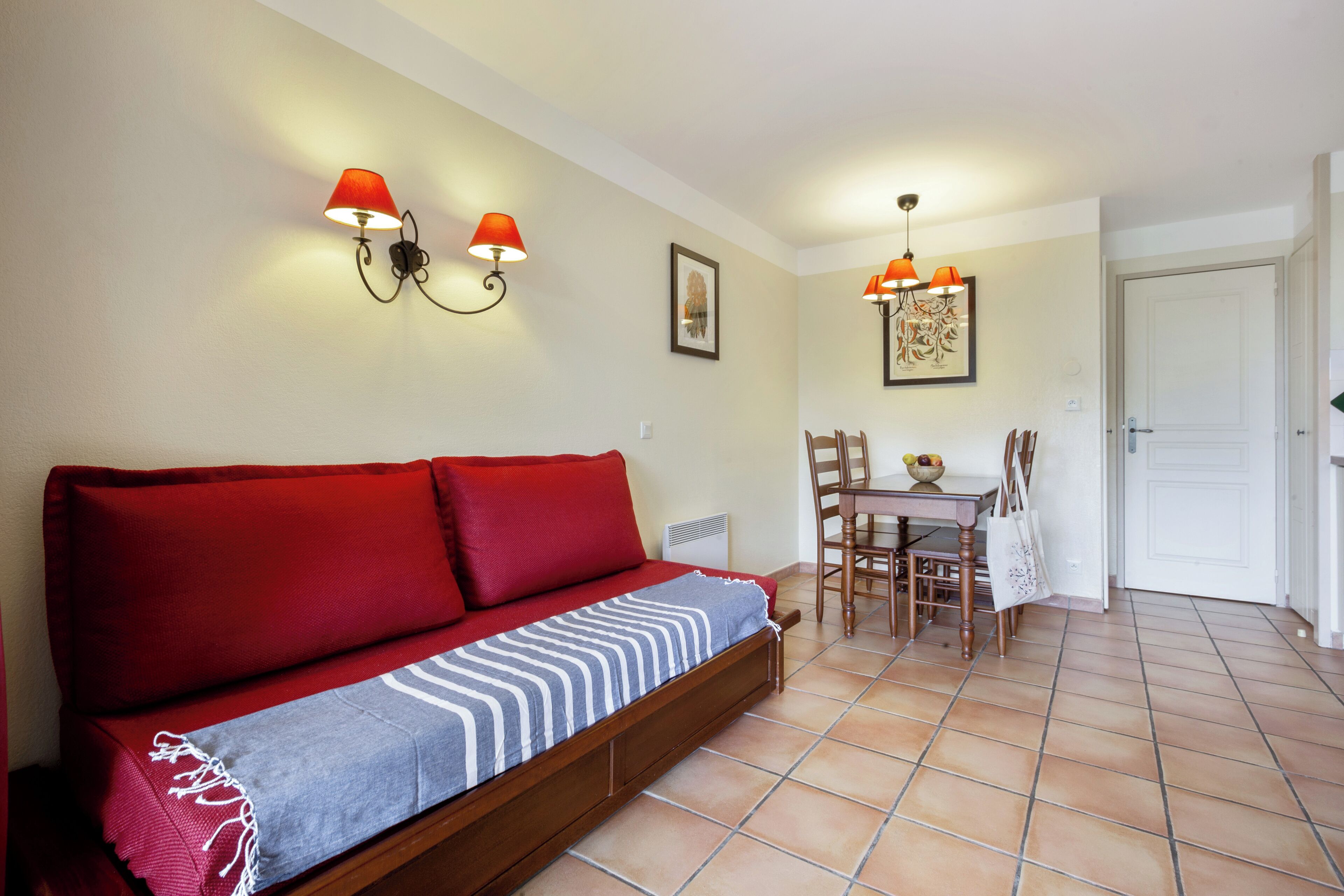 A cozy room with a red sofa, a dining table with chairs, and two wall-mounted lamps.