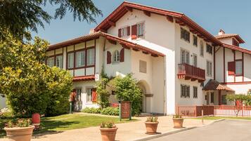 A two-story building with a traditional architectural style, featuring a red-tiled roof and white walls. There are potted plants in the foreground and a signboard in front of the building.