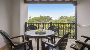A balcony with a round table and four chairs, a bottle, and a glass of water on the table.
