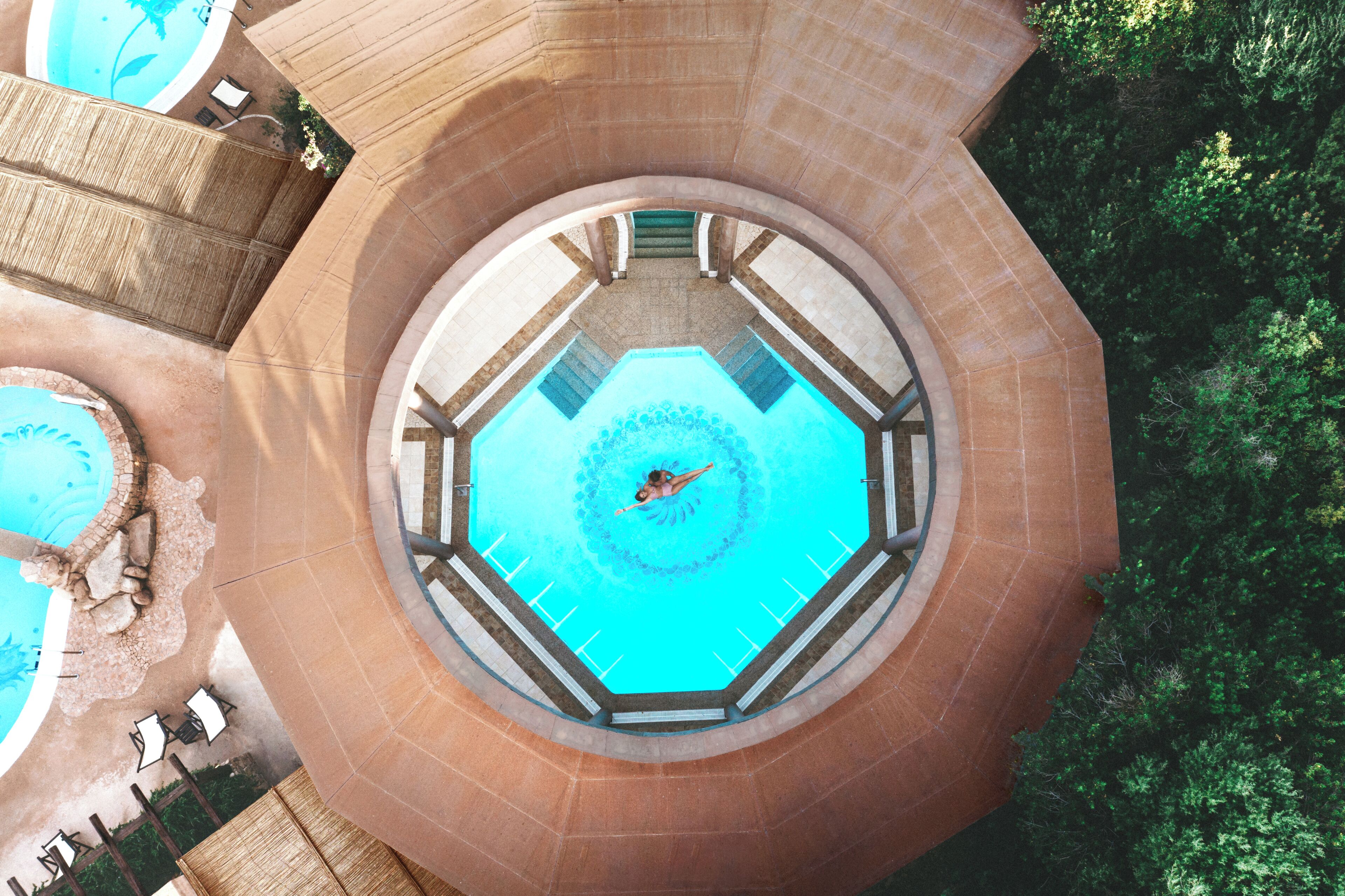 Une piscine circulaire avec une fontaine centrale, entourée d’une structure en pierre aux lignes courbes.