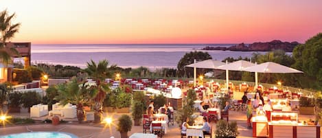 A poolside area with outdoor seating and a view of the sea at sunset.