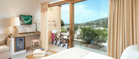 A hotel room with a bed, a desk, a chair, a small table, a sofa, a TV, and a large window with a view of the landscape.