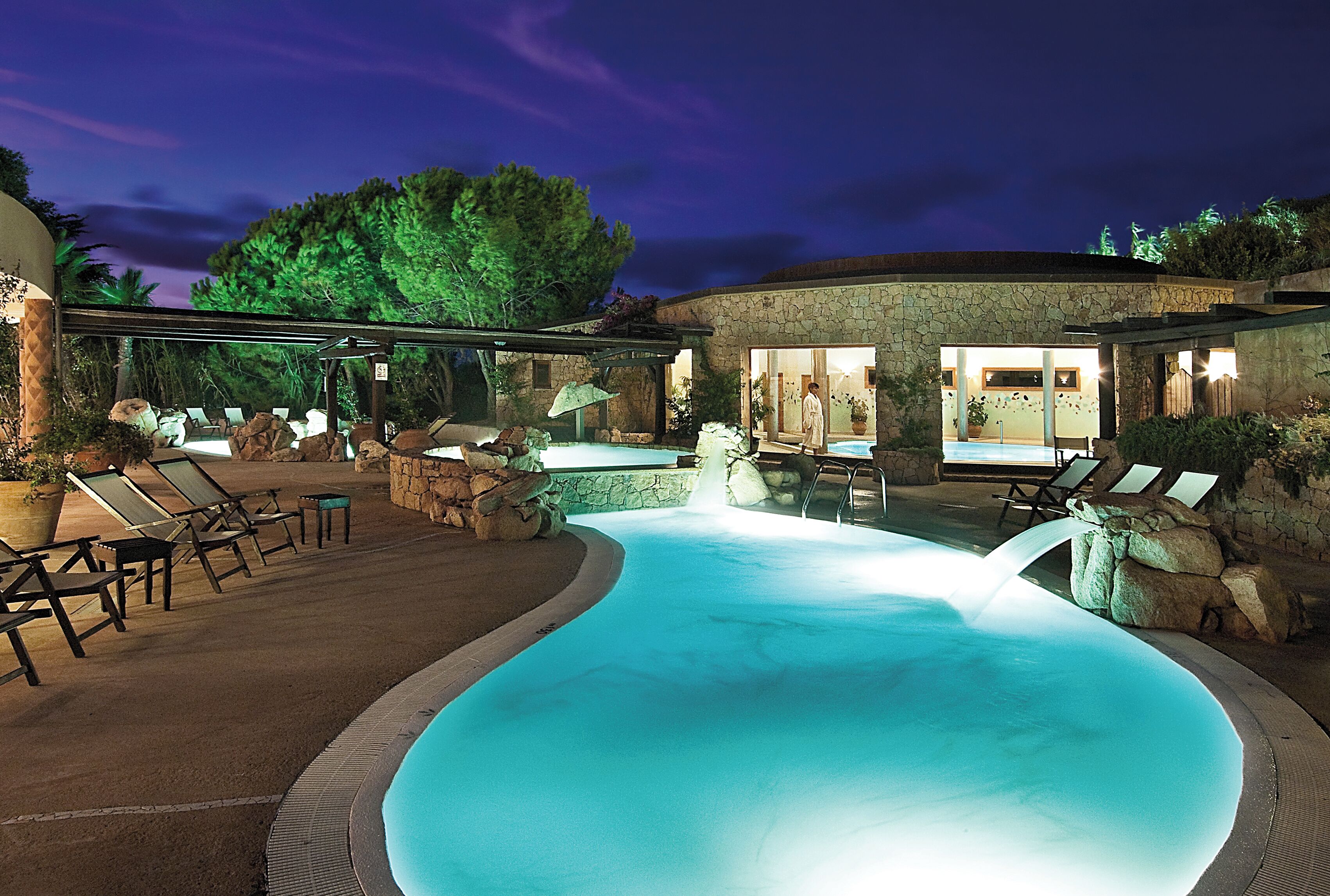 A swimming pool with lounge chairs and a stone building in the background.