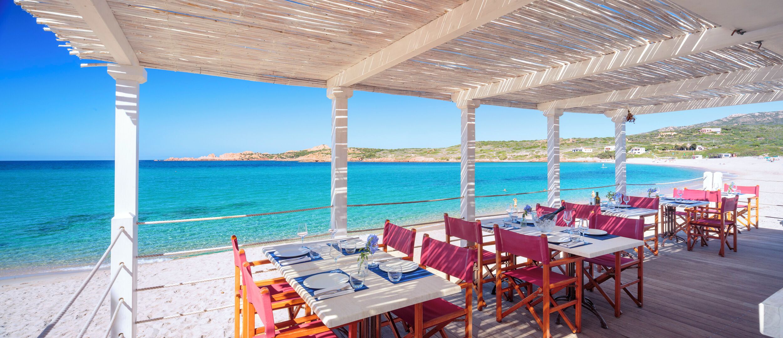 Un espace de restauration en plein air, avec des tables et des chaises, offrant une vue sur une plage et la mer.