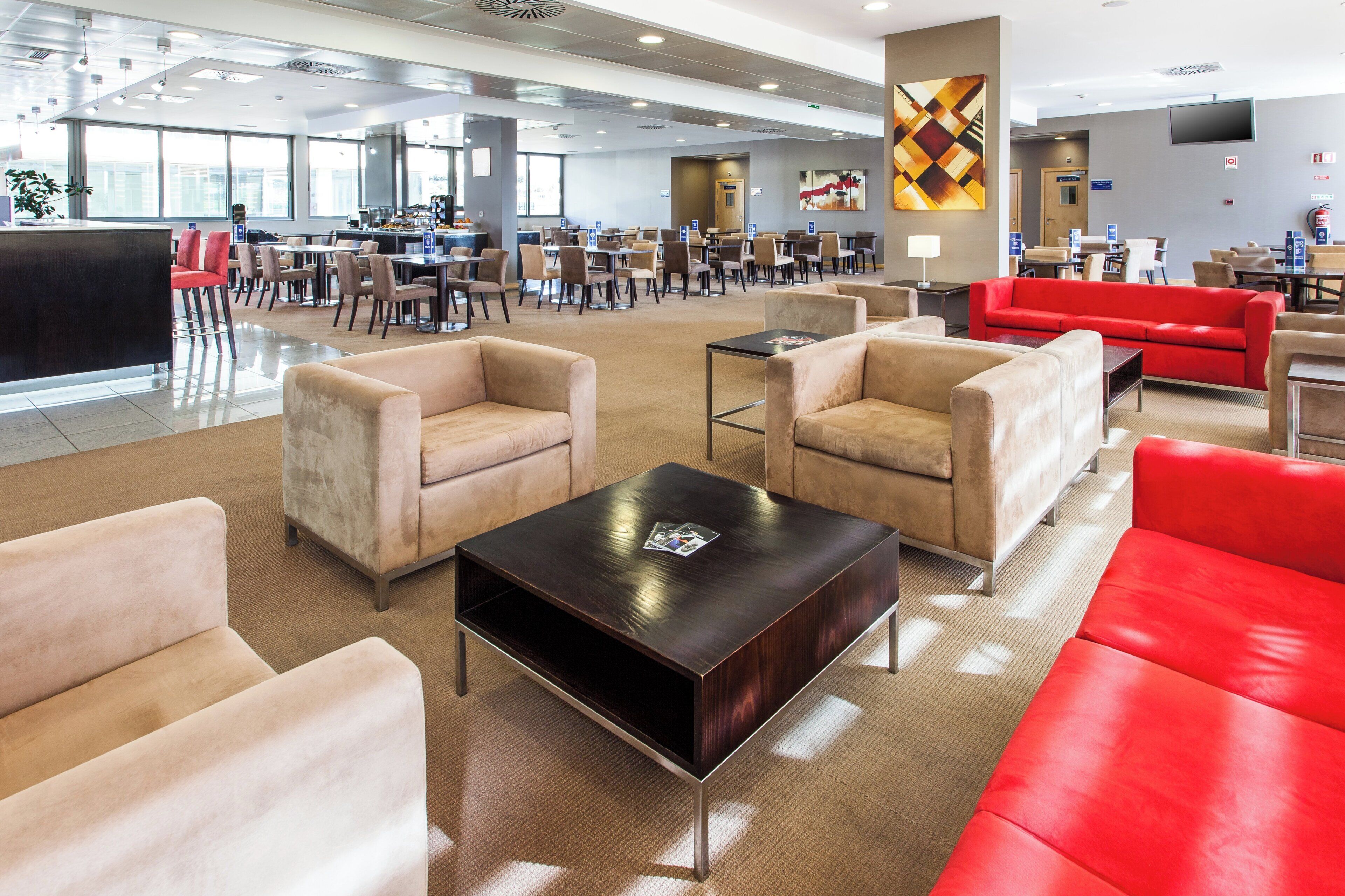 A spacious hotel lobby with multiple seating areas, including sofas and chairs, and a central coffee table.