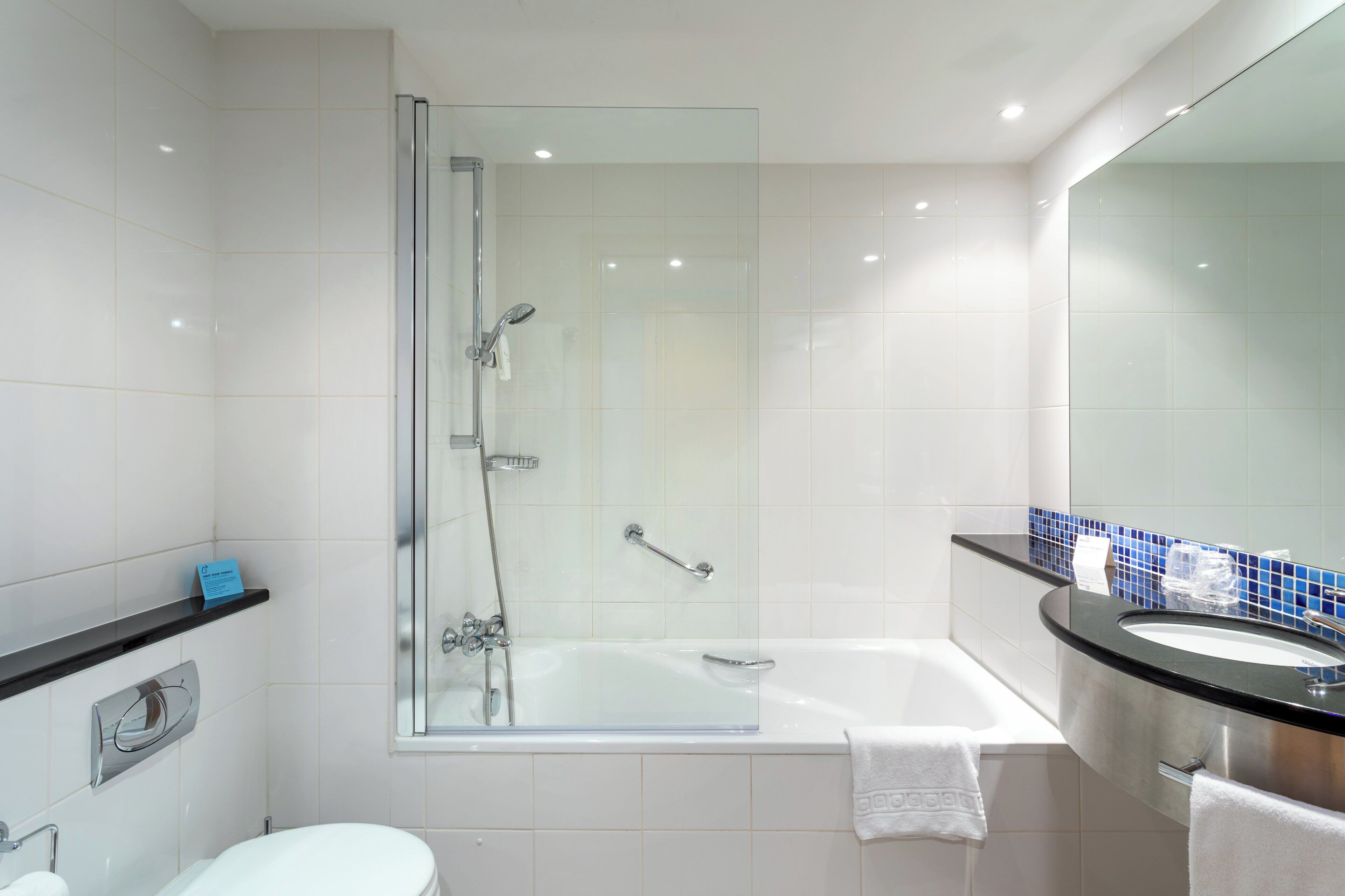A modern bathroom with a glass-enclosed shower, a white bathtub, and a sink with a blue-tiled backsplash.