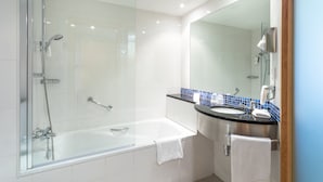 Un baño moderno con ducha envuelta en vidrio, una bañera blanca y un lavamanos con resalte de azulejos azules.