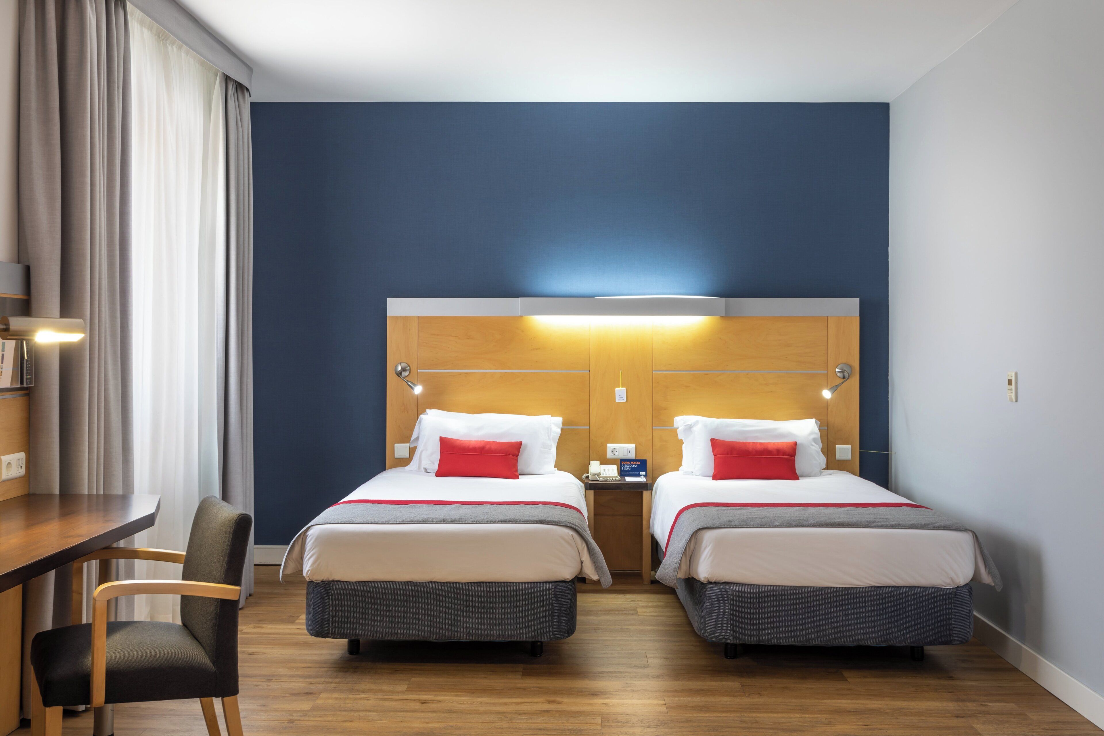 A hotel room with two beds, a desk, and a chair.