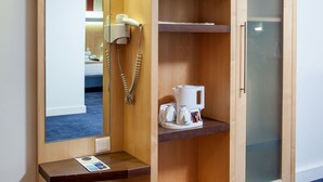 Un armario de madera con espejo, teléfono y repisas con toallas y una cafetera.