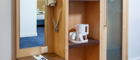 A wooden wardrobe with a mirror, a telephone, and shelves with towels and a coffee maker.