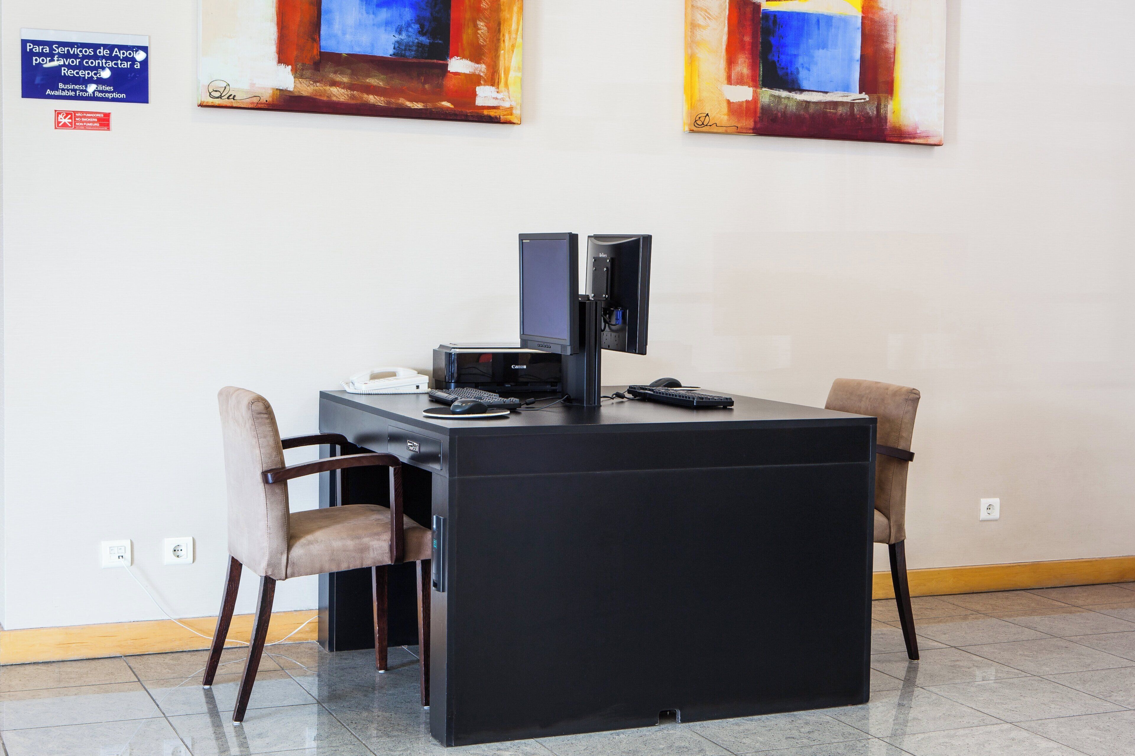 Een receptiebalie met een computer, twee stoelen en een bord aan de muur.