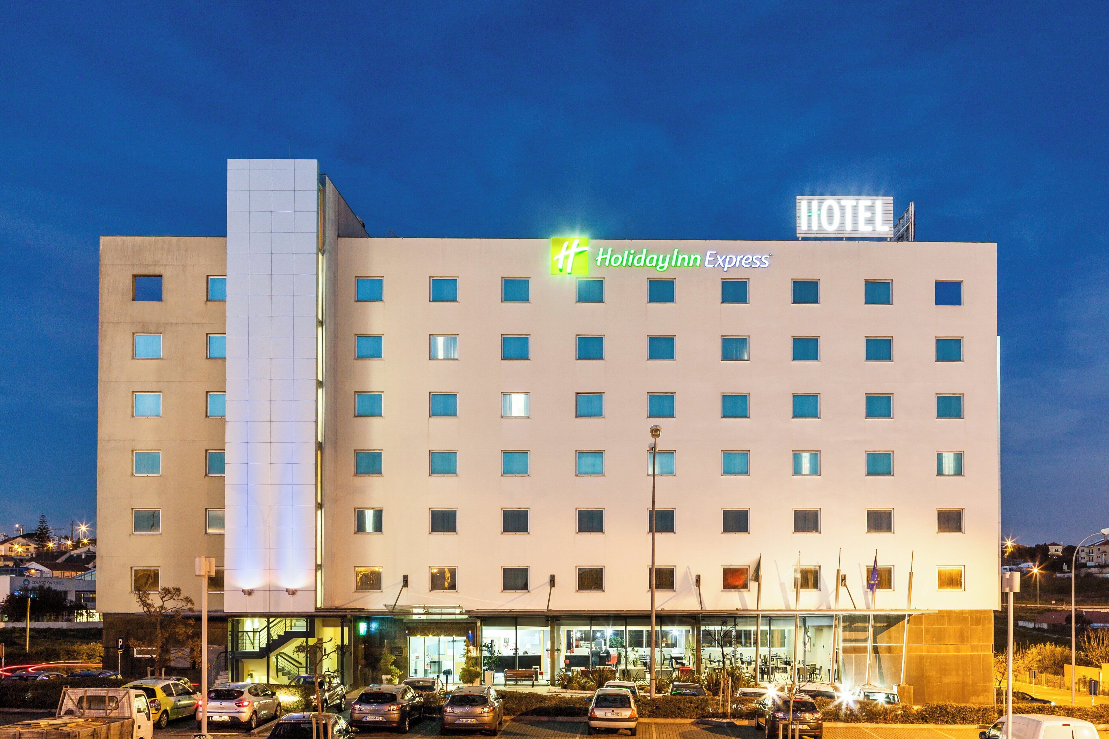 Ein Holiday Inn Express Hotel mit moderner Fassade, zahlreichen Fenstern und einem Parkplatz mit mehreren Autos.