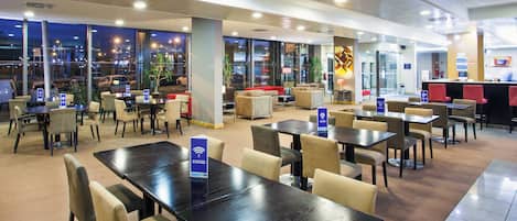 A hotel lobby with multiple seating areas, including tables and chairs, and a reception desk.