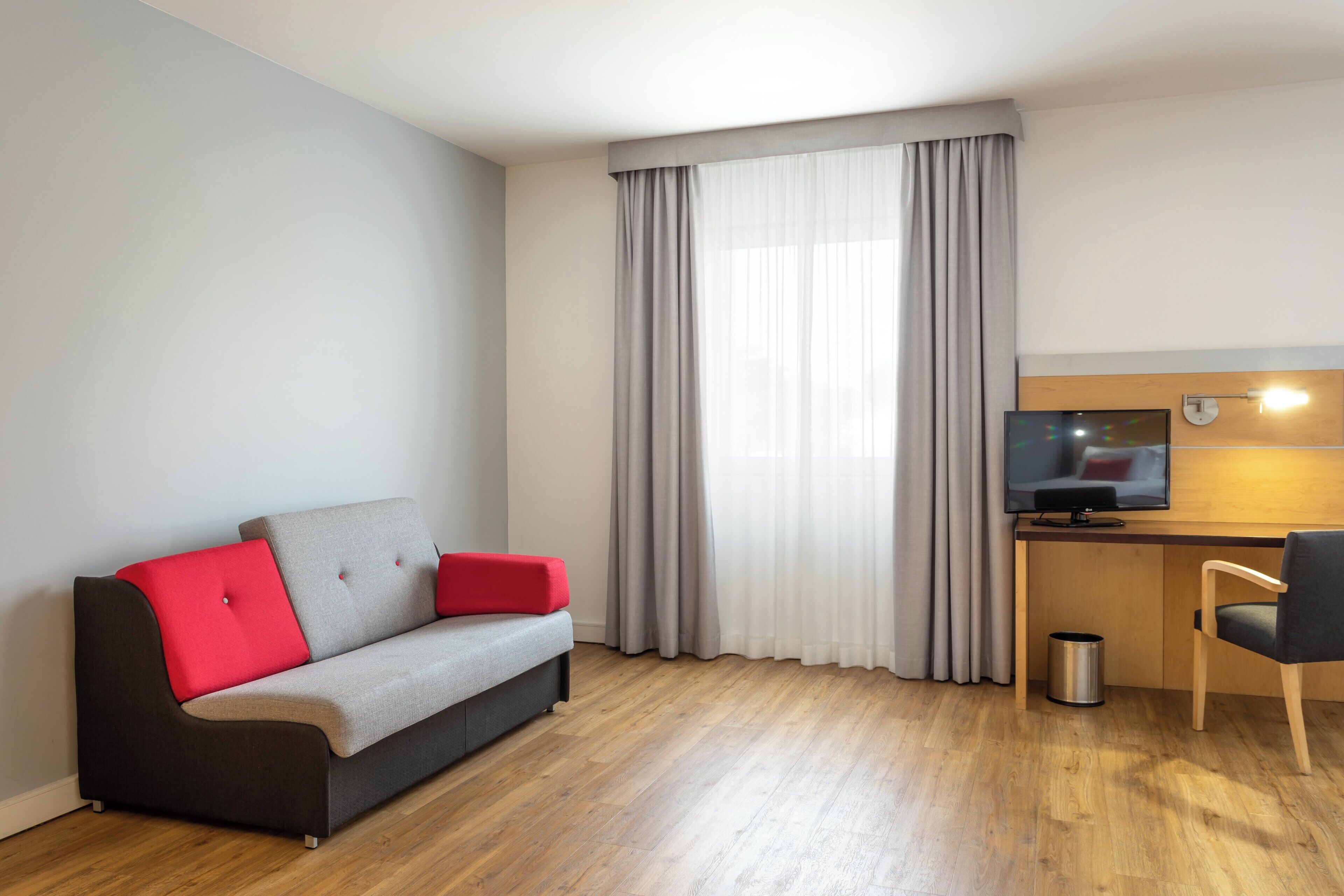 Una sala moderna con un sofá gris, cojines rojos, un escritorio de madera y un televisor, además de una silla.