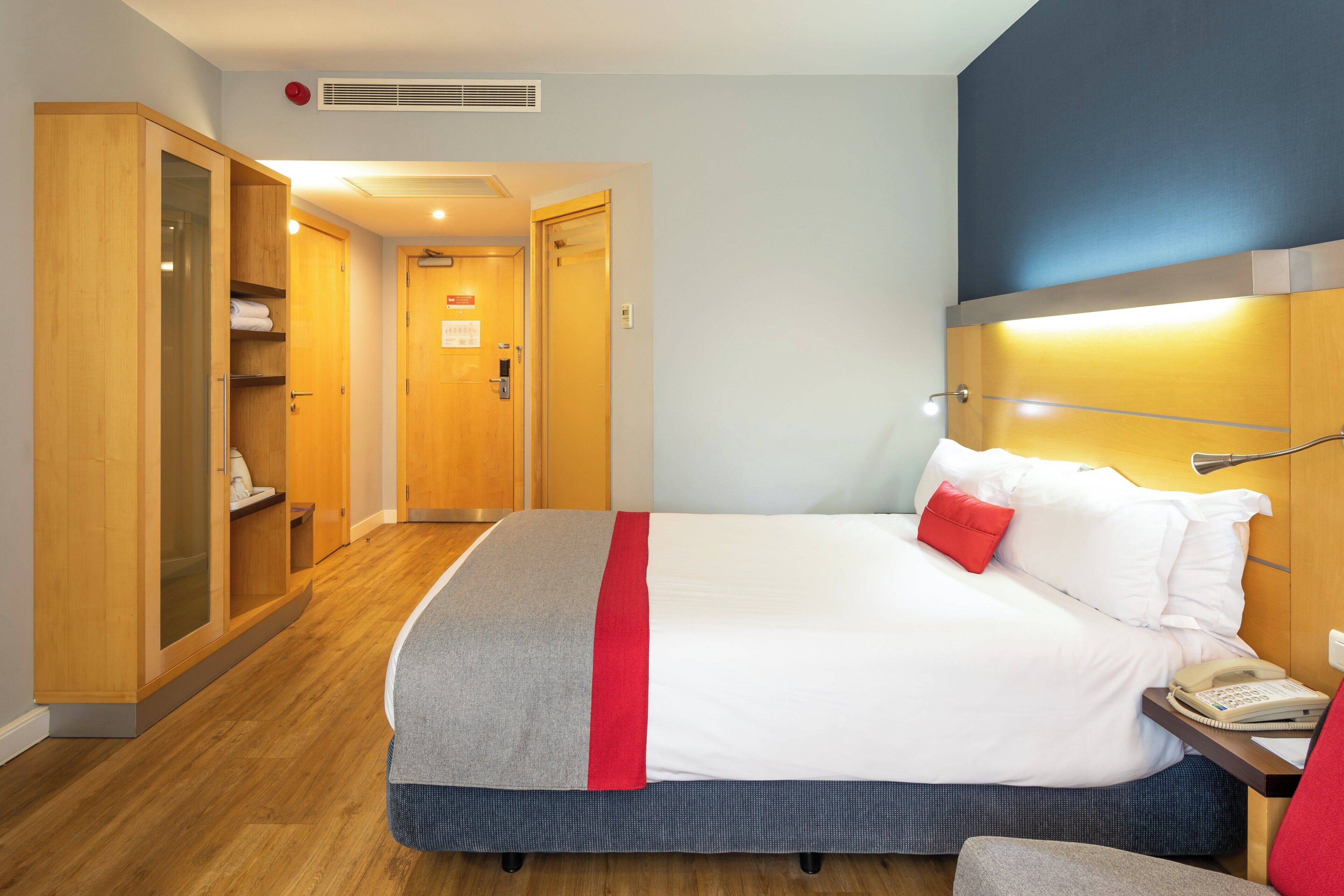 A hotel room with a bed, a bedside table with a telephone, a wardrobe, and a bathroom visible through an open door.