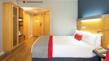 A hotel room with a bed, a bedside table with a telephone, a wardrobe, and a bathroom visible through an open door.