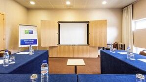 Une salle de conférence équipée d’un grand écran, de tables avec des bouteilles d’eau et d’une pancarte indiquant « Bem-vindo » (Bienvenue).