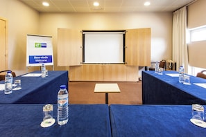 Une salle de conférence équipée d’un grand écran, de tables avec des bouteilles d’eau et d’une pancarte indiquant « Bem-vindo » (Bienvenue).