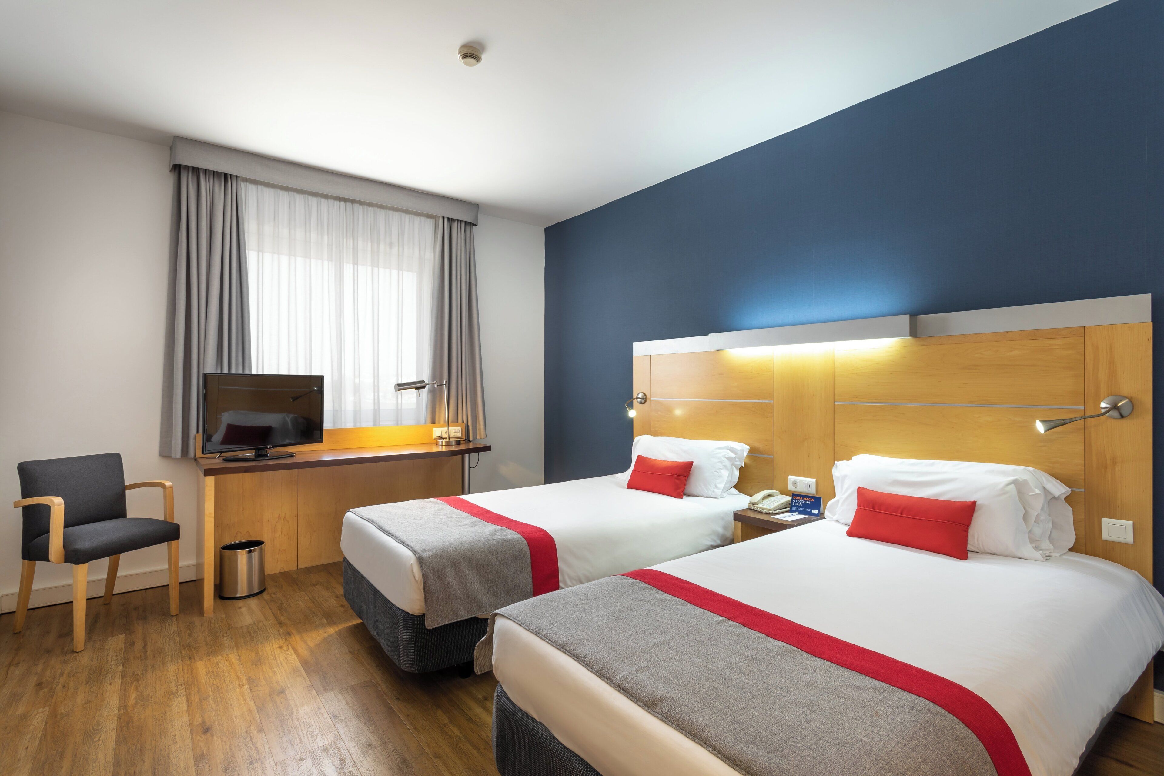A hotel room with two beds, a desk, a chair, and a television.