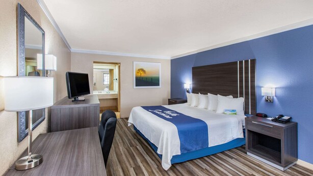 Habitación de hotel con cama, escritorio, televisor y mesita de noche.