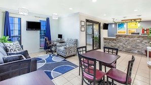 Habitación de hotel con sofá, una mesa de comedor con sillas, televisión y mostrador de recepción.