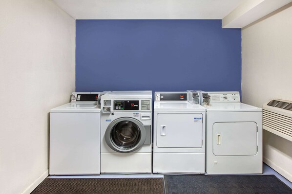 Uma lavanderia com três máquinas de lavar e secar empilhadas, uma parede azul e uma ventilação à direita.
