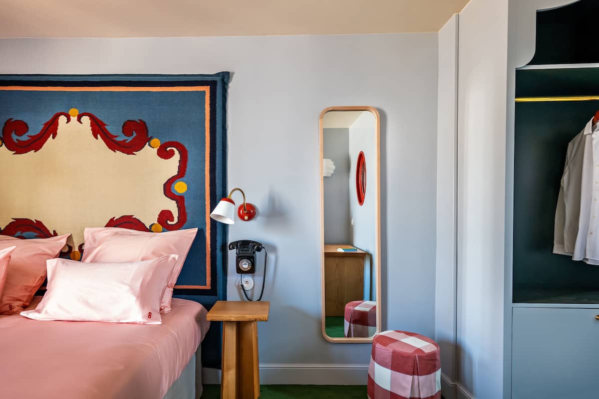Een slaapkamer met een bed, nachtkastje, spiegel, telefoon en een garderobe.