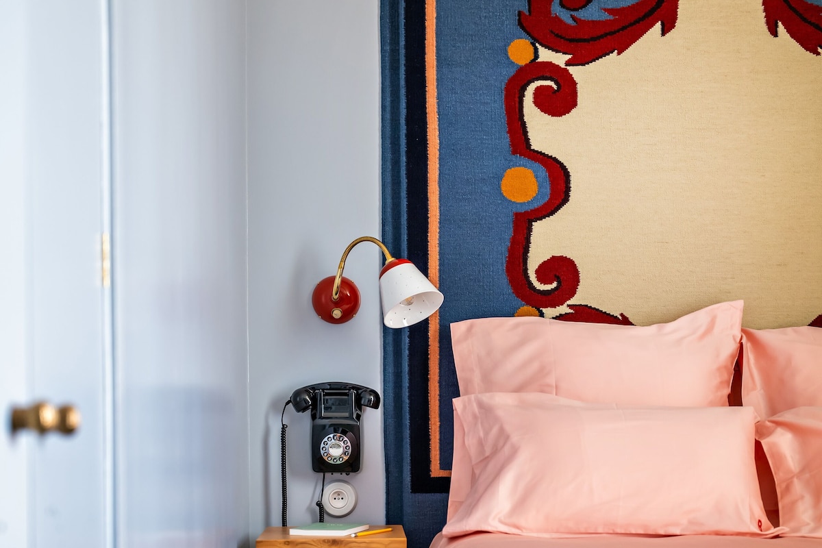 Een slaapkamer met een bed, een nachtkastje met een lamp en een telefoon.