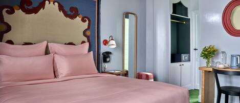 A hotel room with a large bed, a desk with a chair, a mirror, a telephone, and a small table with a vase of flowers.