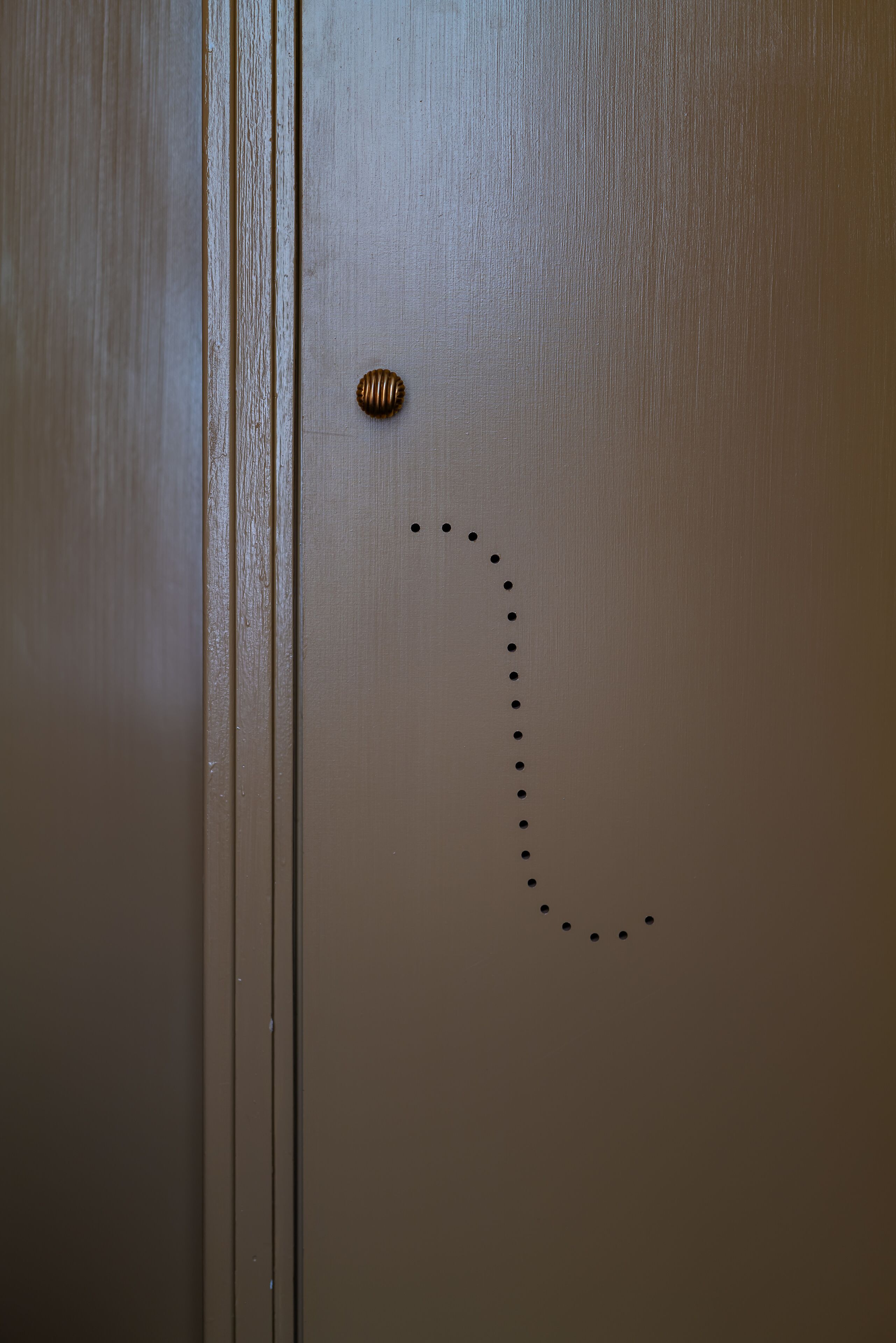 A door with a brass doorknob and a series of evenly spaced holes along the door's surface.