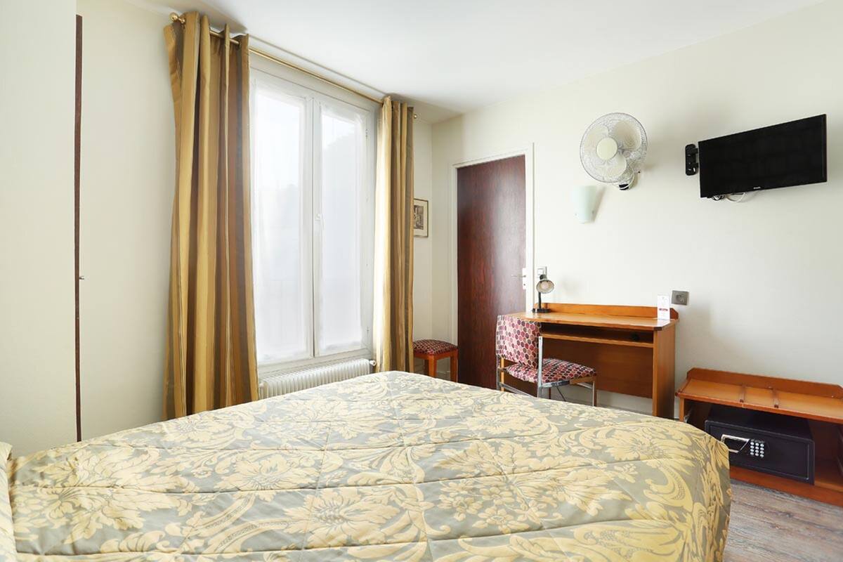 Een slaapkamer met een bed, een bureau, een stoel, een televisie en een ventilator aan de muur.