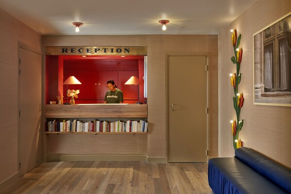 Un área de recepción con un mostrador de madera, una pared roja y una estantería llena de libros.