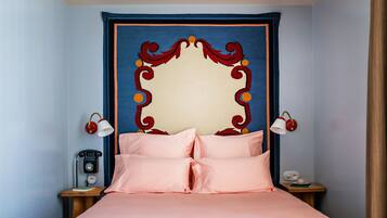 Un letto rifatto con cura, con biancheria rosa, un telefono d'epoca e due lampade a parete sui comodini.