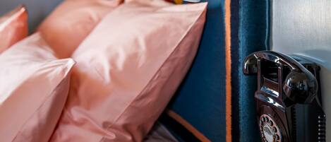 A bed with pink pillows, a red and white lamp, and a vintage telephone on a wall.