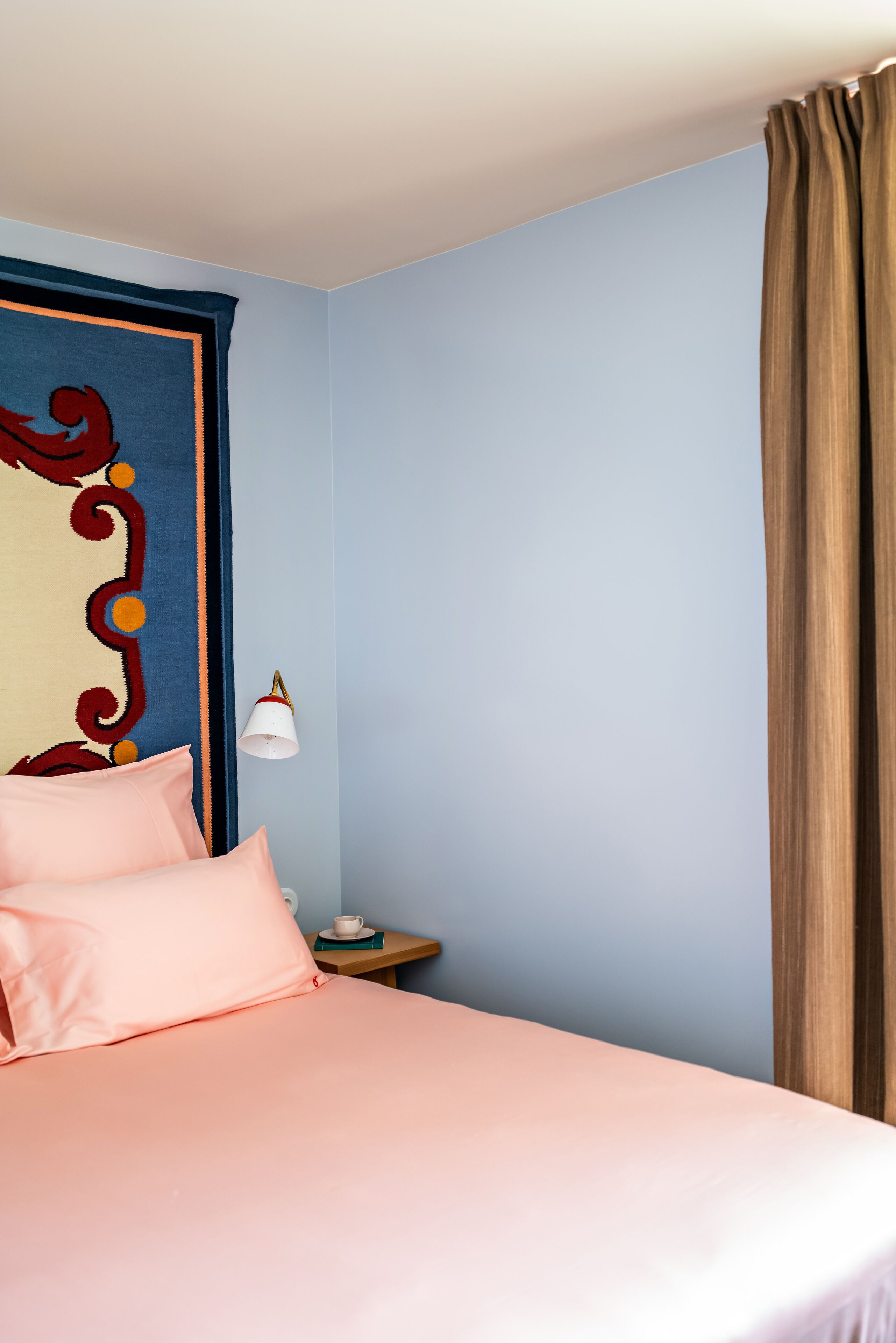 A bedroom with a bed, pillows, a nightstand, a lamp, and a curtain.