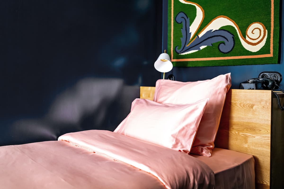 Een bed met roze beddengoed, een houten hoofdbord en een muur met een kleurrijk abstract schilderij.