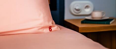 A bed with pink bedding, a white lamp, a red fruit-shaped light, and a small table with a cup and book.