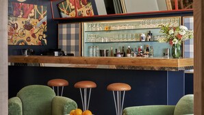 Zona de bar con sillas tapizadas de verde, barra de madera y un espejo decorativo.