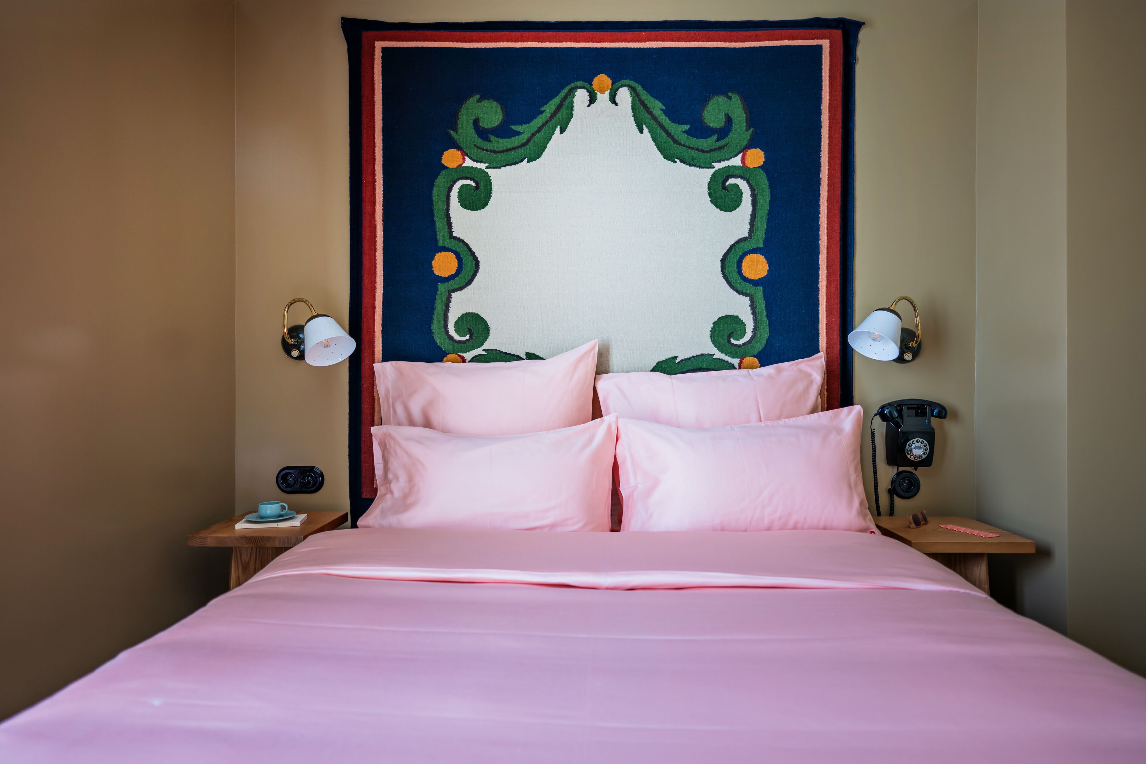 A bed with pink bedding, a decorative headboard, two bedside tables with lamps, and a vintage telephone.