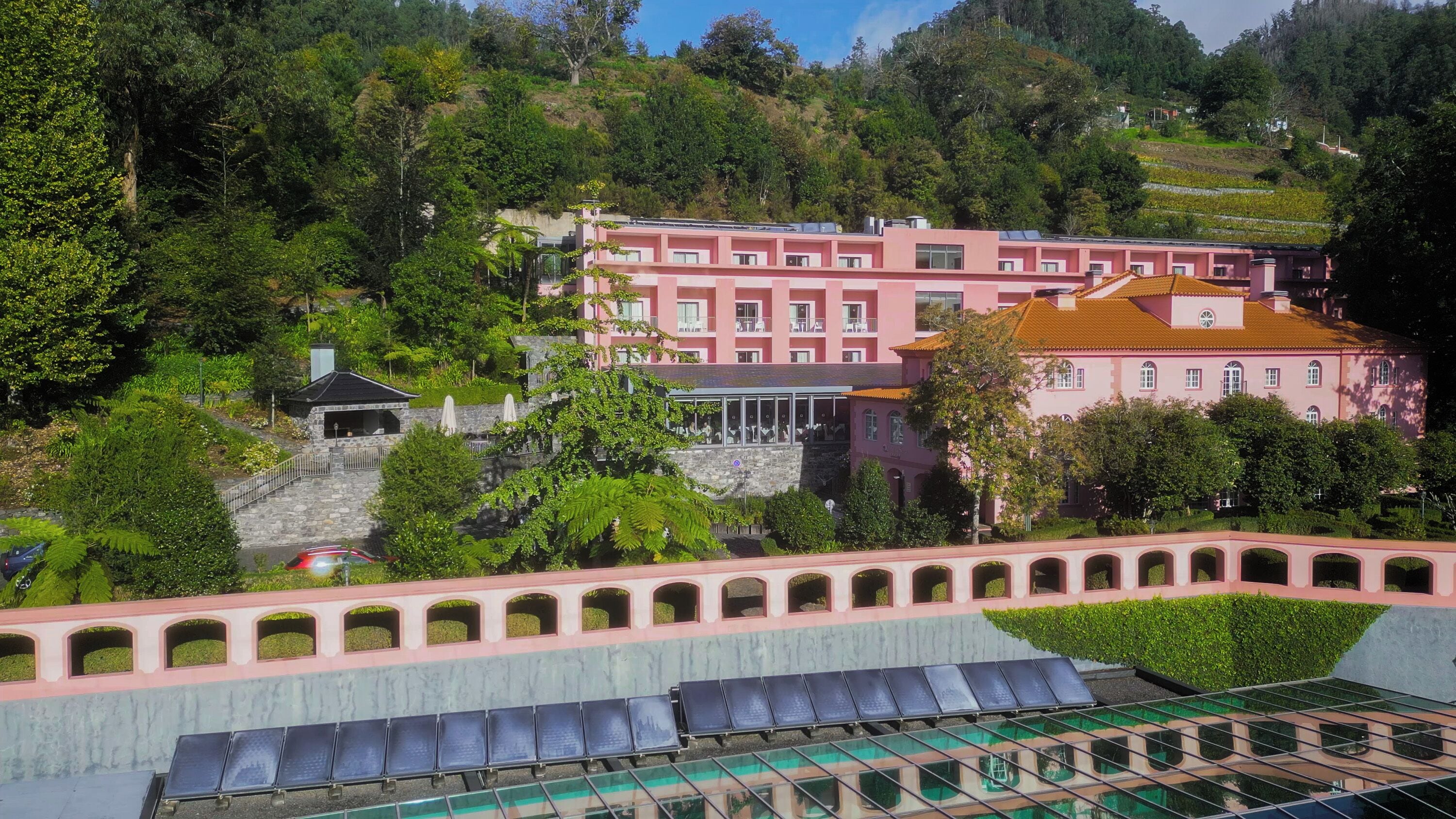 A pink building with multiple balconies, surrounded by lush greenery and a pool area.