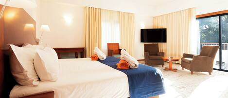 A hotel room with a large bed, a desk, a chair, a TV, and a balcony with curtains.
