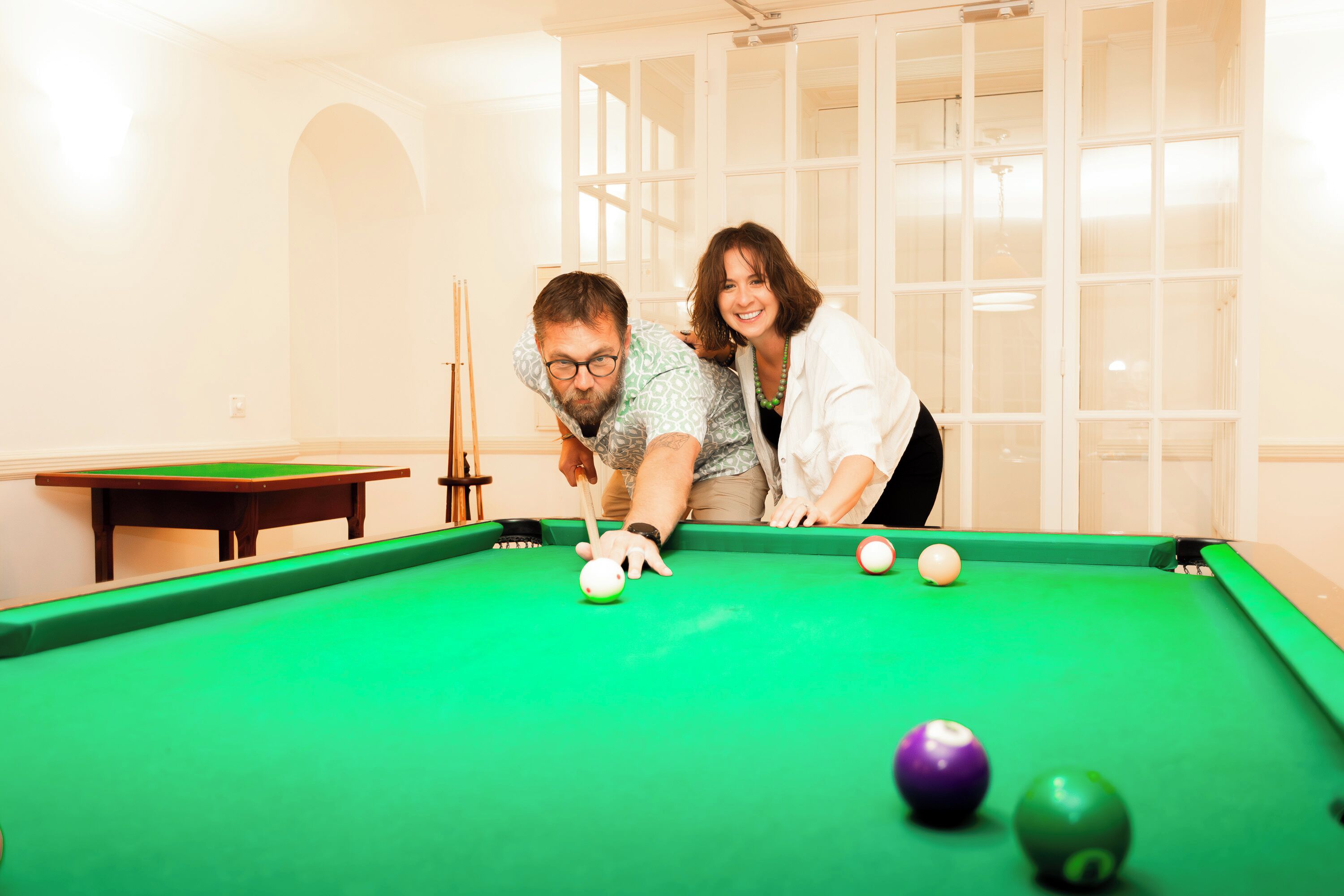 A pool table with balls and a cue stick in a room with a window and a door.