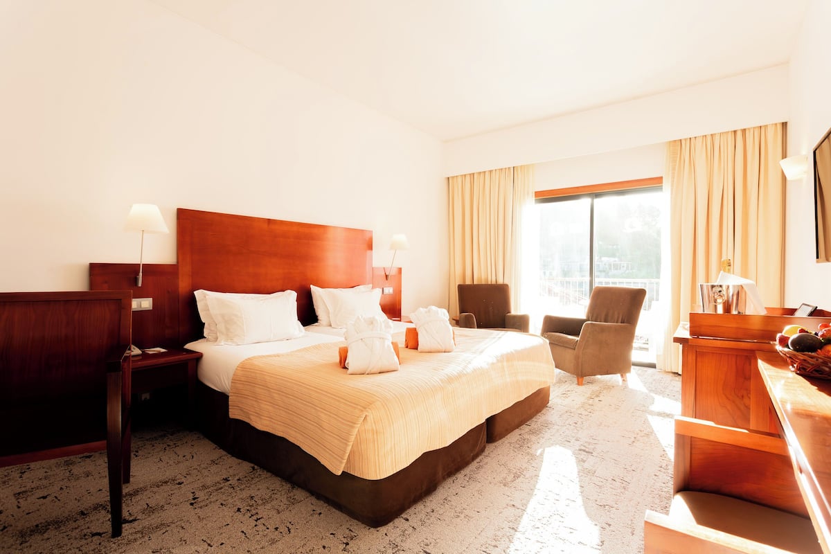 A hotel room with a large bed, a desk, a chair, and a window with curtains.